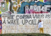 Art student Gregory Borlein prepares his graffito with the inscription "The Corona Virus is a Wake up Call an our Chance to built a new and loving Society" on a wall in the slaughterhouse district in Munich, Germany, Saturday, March 14, 2020. Only for most people, the new coronavirus causes only mild or moderate symptoms, such as fever and cough. For some, especially older adults and people with existing health problems, it can cause more severe illness, including pneumonia. (Peter Kneffel/dpa via AP)